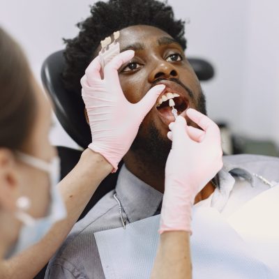 Young african-american man. Guy visiting dentist's office for prevention of the oral cavity. Man and famale doctor while checkup teeth.